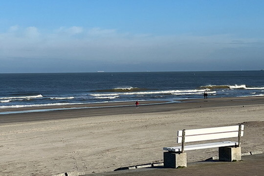 Im Vordergrund ist eine weiße Bank und von dort geht der Blick auf den Strand und das Meer von Norderney