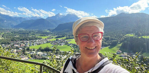 Eine Frau macht ein Selfi und im Hintergrund sind die Berge und kleine Häuser zu sehen