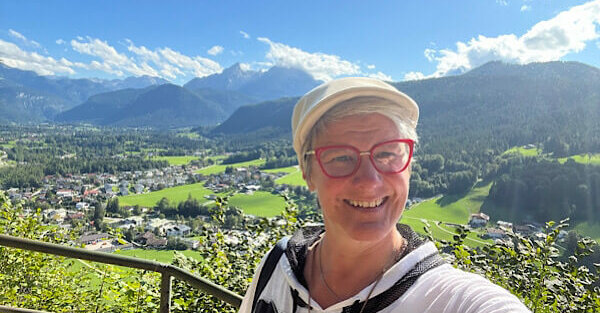 Eine Frau macht ein Selfi und im Hintergrund sind die Berge und kleine Häuser zu sehen