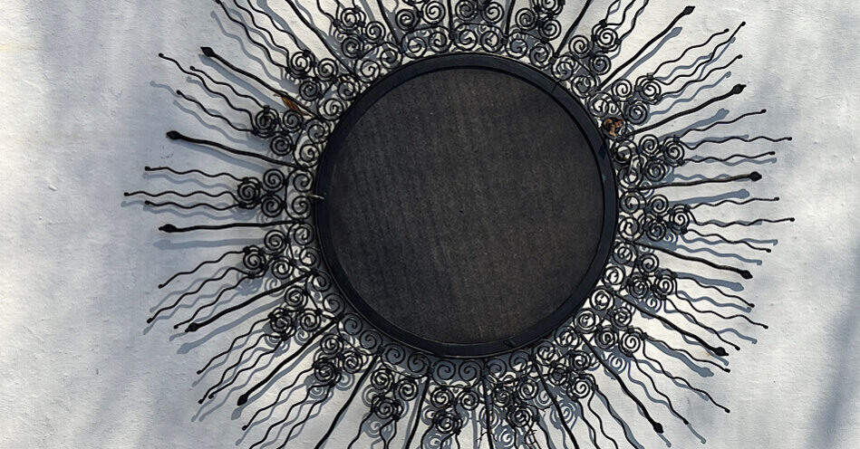 Ein schwarzes, rundes Schild , wovon gerade Strahlen abgehen. Es sieht wie eine Sonne aus.