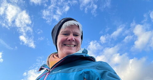 Claudia lacht in die Kamera und über ihr Wolken und blauer Himmel