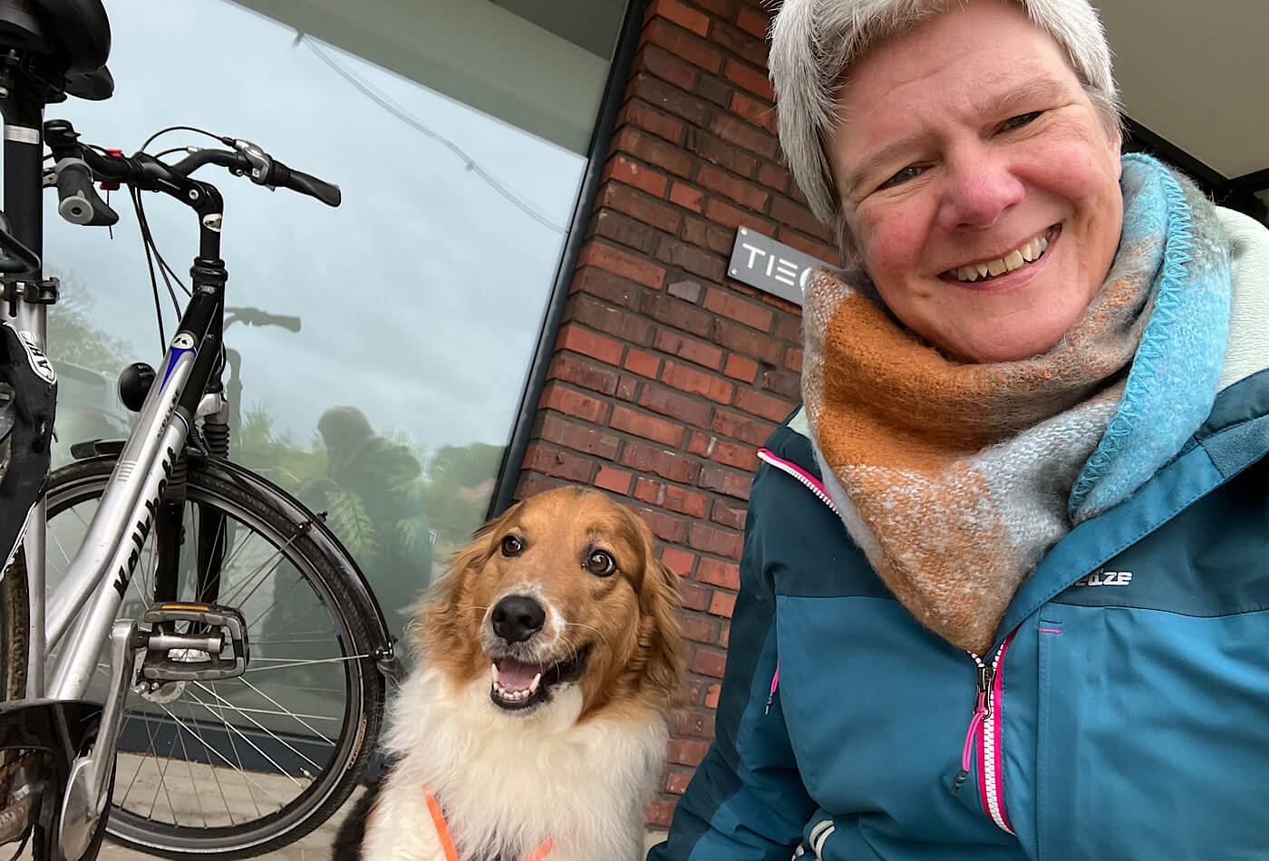 Das Bild zeigt ein Fahrrad und meinen Hund "Frieda" mit mir vor dem Fitnessstudio "Tiegel Gym"