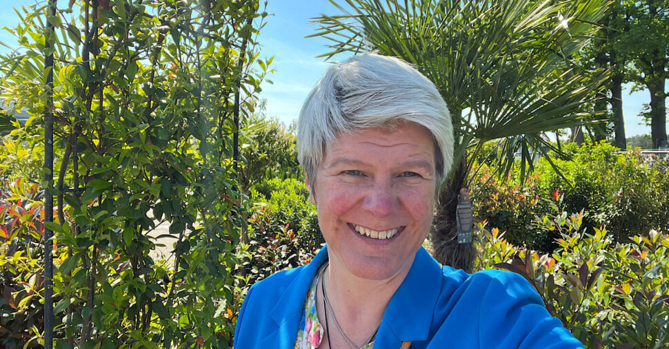 Das Bild zeigt eine Frau im Halbportrait vor einem Dekobogen mit Grünpflanzen im Hintergrund